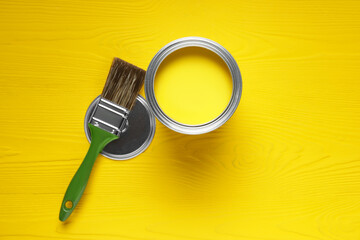 Can of yellow paint and brush on wooden table, flat lay
