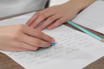 Girl erasing mistake in her notebook at wooden desk, closeup