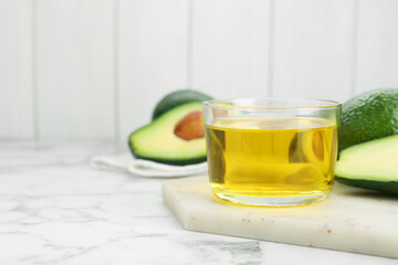 Bowl with oil and fresh avocados on white marble table, closeup. Space for text