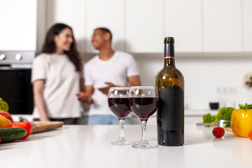 young happy multiracial couple drinking wine in white modern kitchen, mock up bottle with blank label
