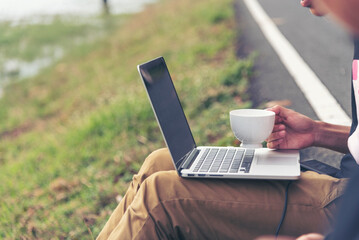 Man hands typing laptop notebook holding coffee cup outside office. Close up man hands using computer laptop sit on green park outdoors lifestyle. freelancer Men using laptop home office technology