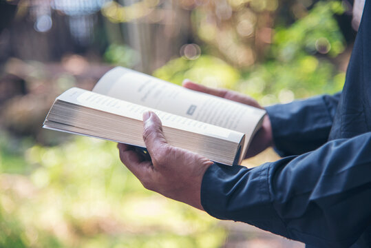 Asian man holding book reading magazine at green park in natural garden. Young man relaxation read open book self study. University men happy learning. Closeup Men hands open textbook in green park