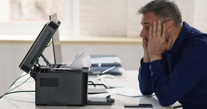 Irritated Businessman Looking At Paper Stuck In Printer