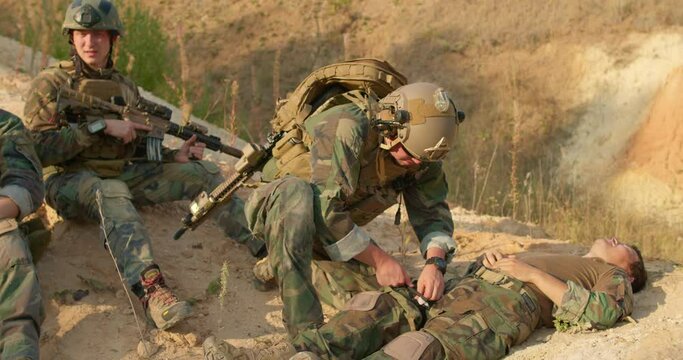 soldier is listen to heartbeat and take pulse of his friend while he is lying on the ground with painful leg and arm, slow motion