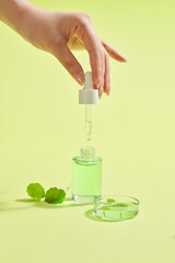Vertical image of pipette with cosmetic serum in women's hands on light green background, fresh...