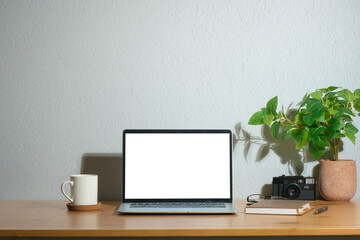 Laptop computer with empty screen, coffee cup, houseplant and camera on wooden table.