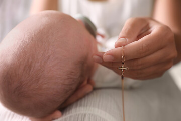 Obraz na płótnie Canvas Mother holding Christian cross near newborn baby indoors, closeup