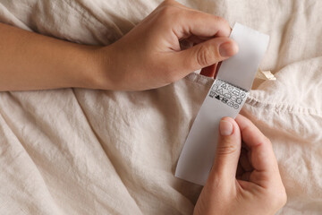 Woman holding clothing label on beige garment, closeup