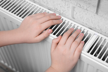 Girl warming hands on heating radiator indoors, closeup