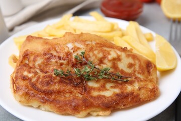 Tasty soda water battered fish, potato chips and lemon slice on plate, closeup