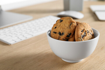 Chocolate chip cookies on wooden table at workplace, closeup. Space for text