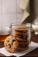 Glass jar with delicious chocolate chip cookies and tea on wooden table