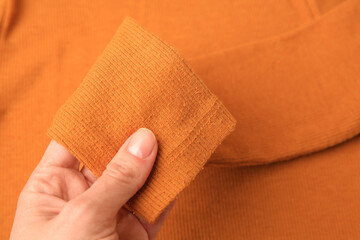 Woman holding sleeve of orange sweater with lint as background, top view. Before using fabric shaver