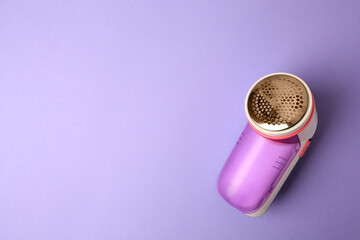 Modern fabric shaver on violet background, top view. Space for text