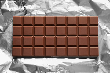 Delicious milk chocolate bar on foil, top view