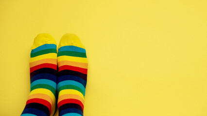legs in rainbow socks and on a monochrome yellow background, a layout with a place for text and a place to copy. pair of rainbow-colored socks. Symbol LGBT