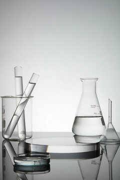 Test tubes, petri dish and erlenmeyer flask containing water, transparent podium in round shape with empty space for product presentation. Laboratory concept
