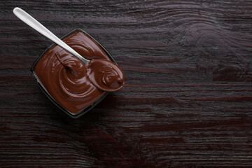 Bowl with tasty chocolate paste and spoon on wooden table, top view. Space for text