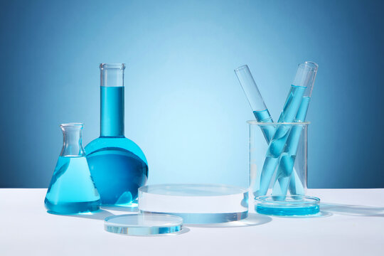 Front view of circle transparent podium and laboratory glassware filled with blue water. Empty area to display product. Concept of chemical, scientific experiment