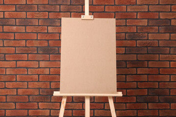 Wooden easel with blank board near brick wall - obrazy, fototapety, plakaty