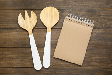 Blank recipe book and kitchen utensils on wooden table, flat lay. Space for text