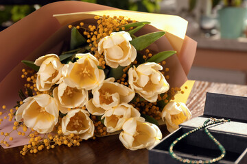 Bouquet with beautiful tulips, mimosa flowers and box of jewelry on wooden table indoors