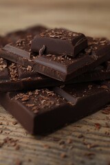 Pieces and shavings of tasty chocolate on wooden table, closeup