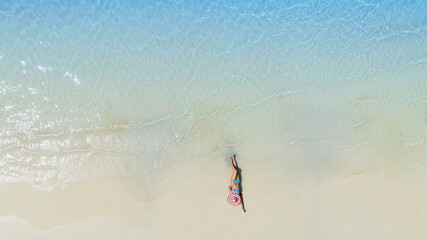 Aerial view with woman  in bikini sunbathing as laying on the beach, blue sea water in background