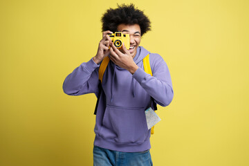 Young smiling African American photographer taking pictures isolated on yellow background