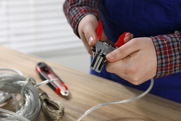 Fototapeta premium Professional electrician stripping wiring at wooden table, closeup view