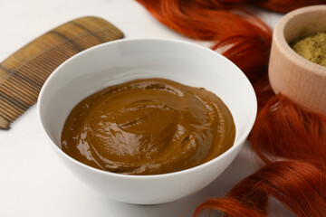 Bowl of henna cream and red strand on white table, closeup. Natural hair coloring