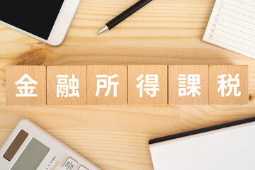 金融所得課税と書かれたブロック、電卓、スマホ、ノート、カレンダー