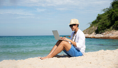 man using and typing on laptop computer while sitting on the beach