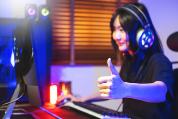 Happy asia girl gamer wear headphone competition play video game online with computer colorful neon light in living room at night