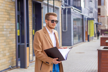 Portrait of a handsome man, businessman, scientist or teacher. He walks along a modern city street with a folder of documents and a notebook in his hands