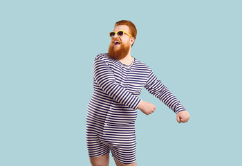 Funny bearded chubby man in sailor leotard having fun on pastel light blue background. Humorous redhead fat man in striped clothes and sunglasses laughs making dance moves. Fun concept. Banner.