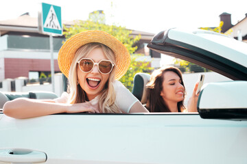 Portrait of two young beautiful and smiling hipster female in convertible car. Sexy carefree women...