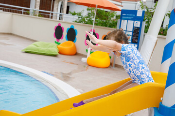 Little preschool girl sliding on a children slide in outdoor swimming pool in hotel resort. Child...