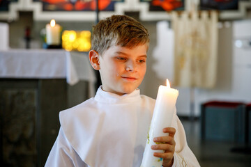 Little kid boy receiving his first holy communion. Happy child holding Christening candle....