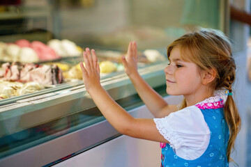 Cute little preschool girl choosing and buying ice cream in outdoor stand cafe. Happy smiling child...