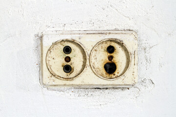 An old burned-out outlet in the wall. Dirty socket in the wall of white plaster.