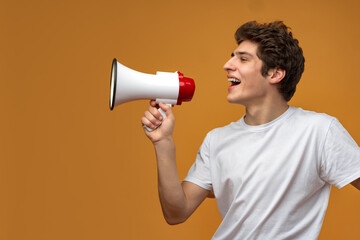 Young man shouting into megaphone making announcement against yellow background