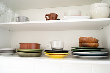 Multicolored dishes on a shelf in a white kitchen cabinet.