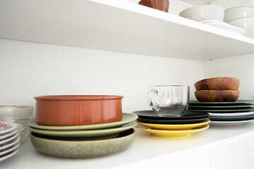 Multicolored dishes on a shelf in a white kitchen cabinet.