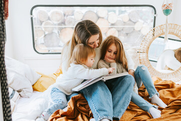 family mom and two red haired cute girl little daughters having fun and reading book in cosy bed in...