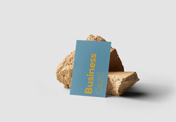 Mockup of customizable vertical color business card resting against rocks available against customizable color background