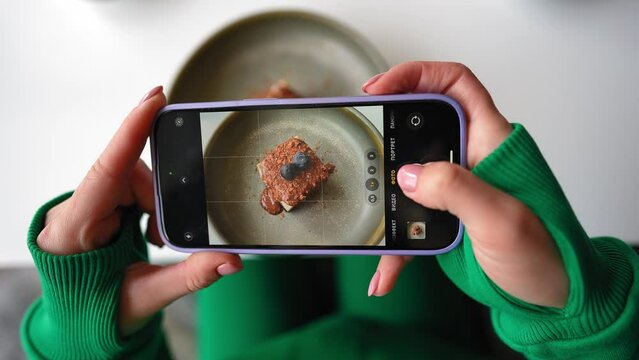 Influencer or Blogger Filming His Breakfast on a Smartphone in a Cafe Restaurant and Sharing on Social Media. Female Hands Take Pictures of Food Using a Mobile Phone Close-up. Slow Motion. Top View.