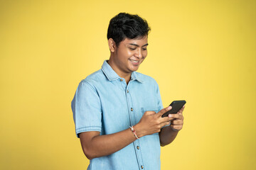 young Asian man smiles using a smartphone in an isolated background