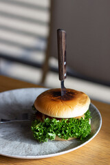Big grilled vegan hamburger with green fresh salad on trendy gray plate, wooden table in cafe. Fast food concept.