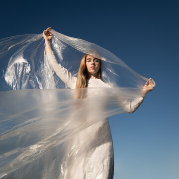 woman in white dress under blue sky with sheet of thin plastic foil